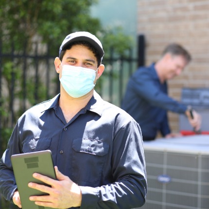 Hvac Tech Standing In Front Of Unit Holding Clipboard